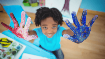 happy kid holding up messy hands with paint on them