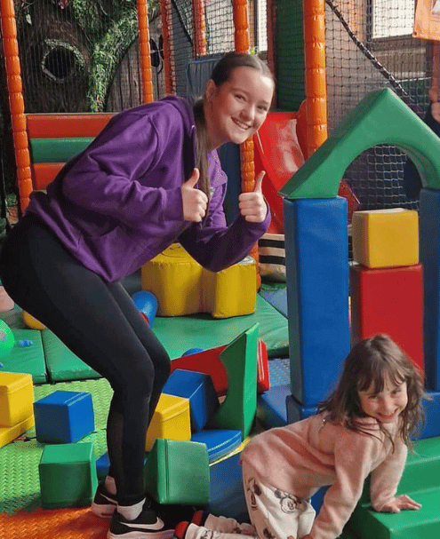 Charlie Park play worker giving the thumbs up with a young girl playing by her feet.